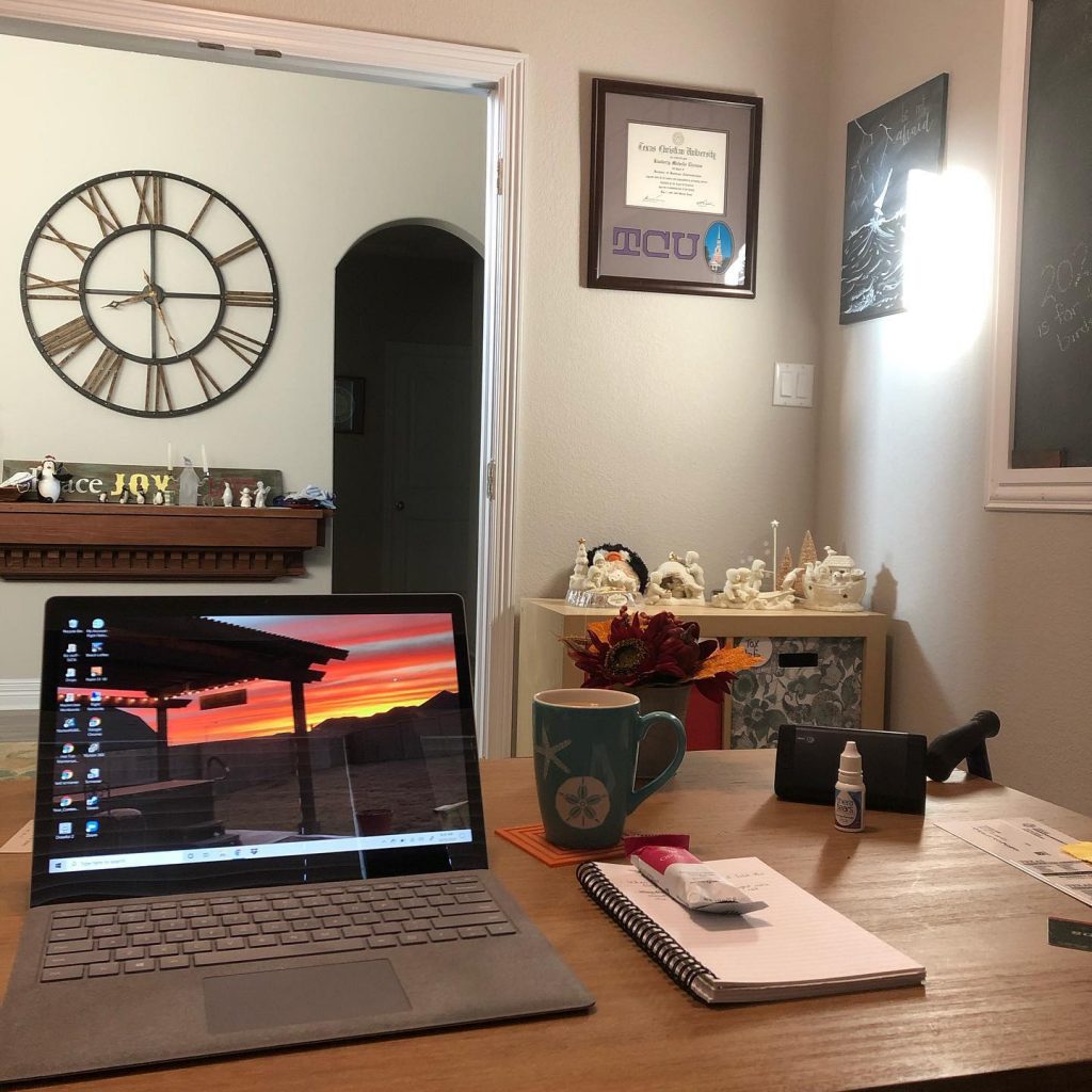Computer open on desk, a large clock on the wall outside office doorway large