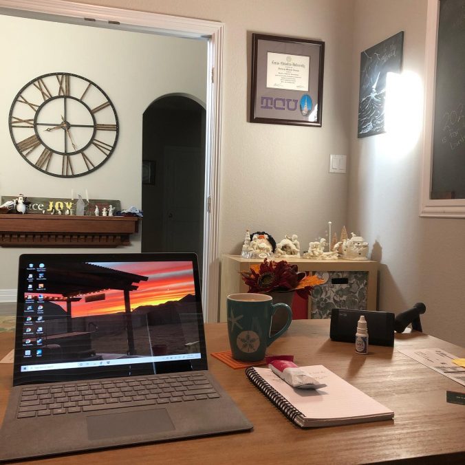 Computer open on desk, a large clock on the wall outside office doorway large